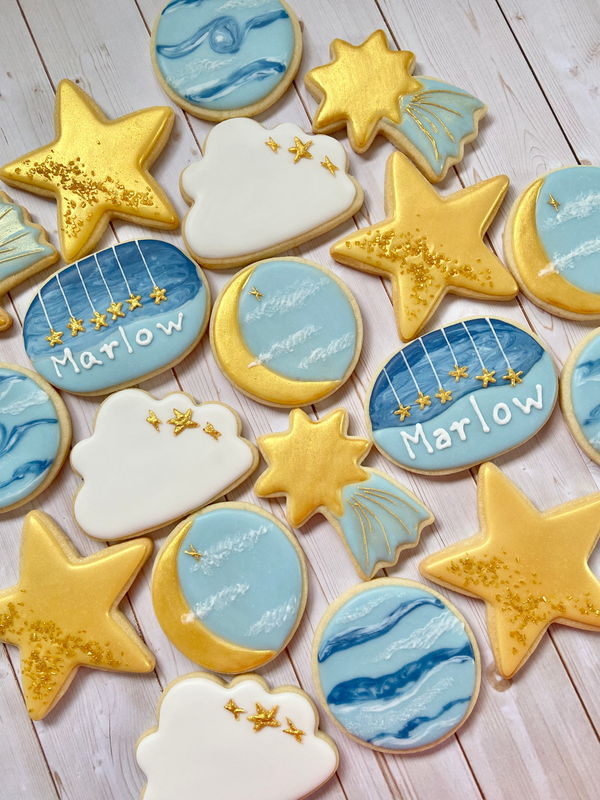 Decorative cookies shaped like stars, moons, and clouds with 'Marlow' written on them, arranged on a wooden surface.