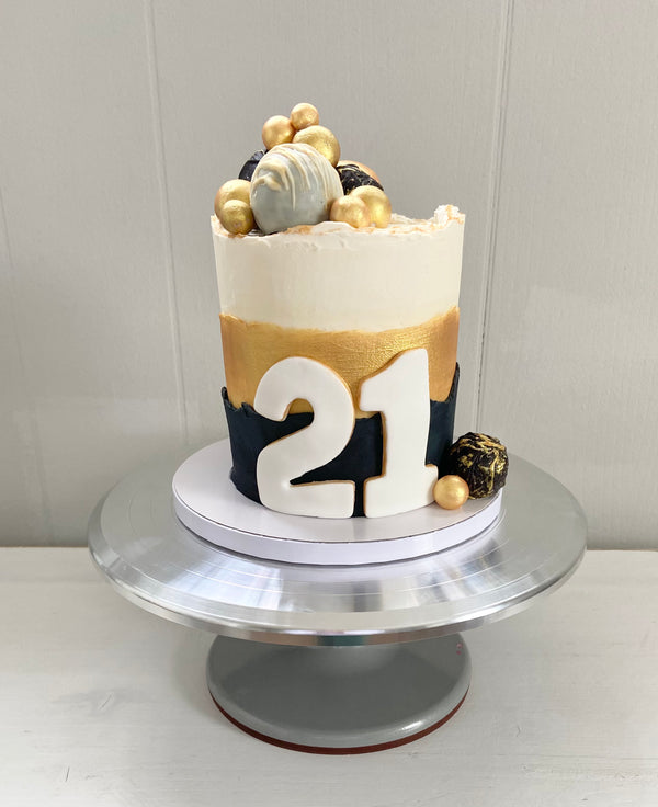 Single tier cake with black and metallic gold buttercream on the sides. Fondant 21 on side, and black, gold and white truffles on top and bottom border.