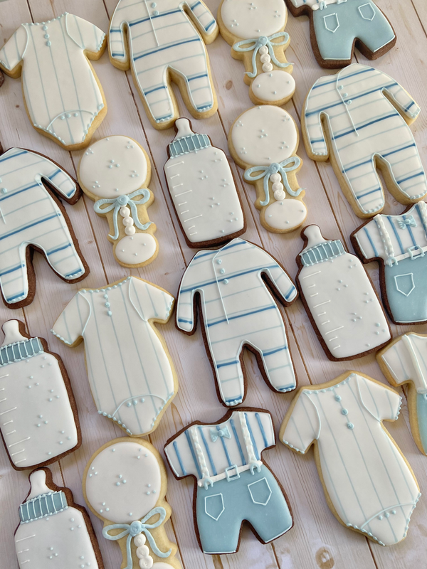 Cookies shaped like baby onesies, bottles, and pacifiers on a wooden surface