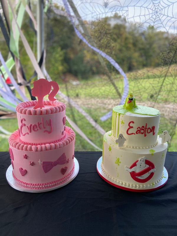 Two cakes, each two tiered. Pink Barbie cake with Barbie silhouette topper and bows and hearts on sides. Ghost Busters cake with slime topper, and ghosts on sides.
