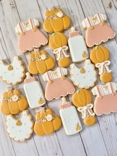 Baby shower decorated cookies shaped like dresses, bottles, rattles, bibs, and pumpkins.