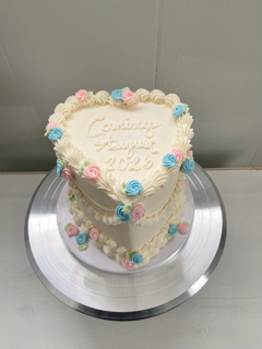 Heart shaped cake with white icing and decorative flowers on a silver cake stand.