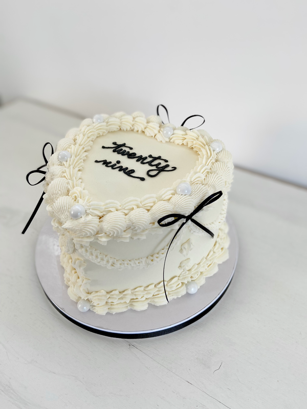 White cake with decorative piping, black bows, and age written in black icing.