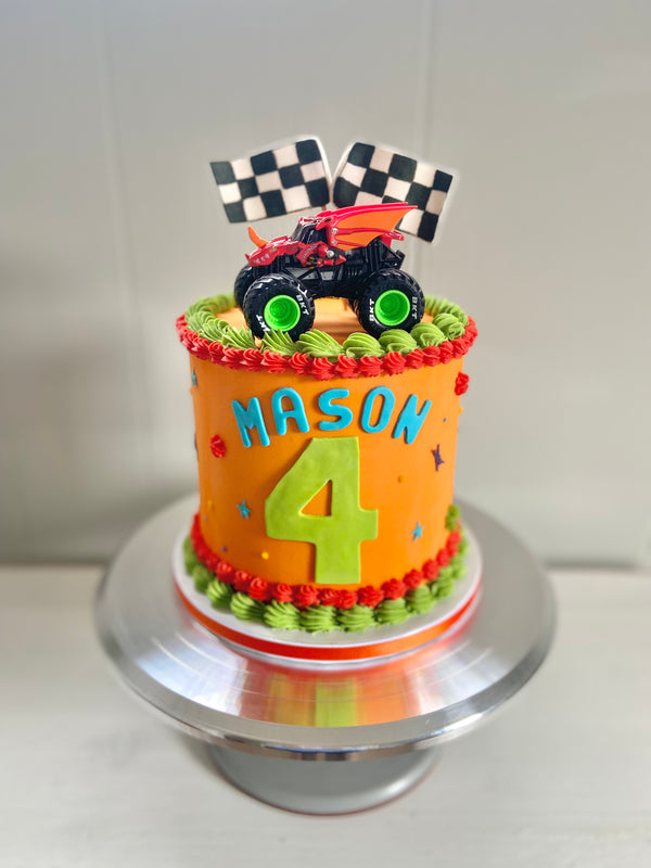 Orange cake with lime green and red piping. Monster truck topper with checkered racing flags.