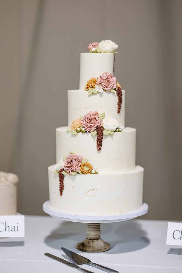 Four tiered wedding cake with fall colored buttercream flowers on the ledges of each tier.