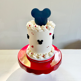 Small white cake with Mickey Mouse design on a red cake stand against a white background