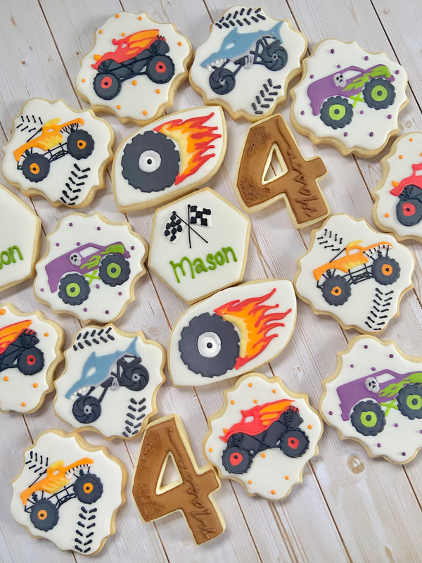 Decorative cookies with monster truck designs and the number 4 on a wooden surface.