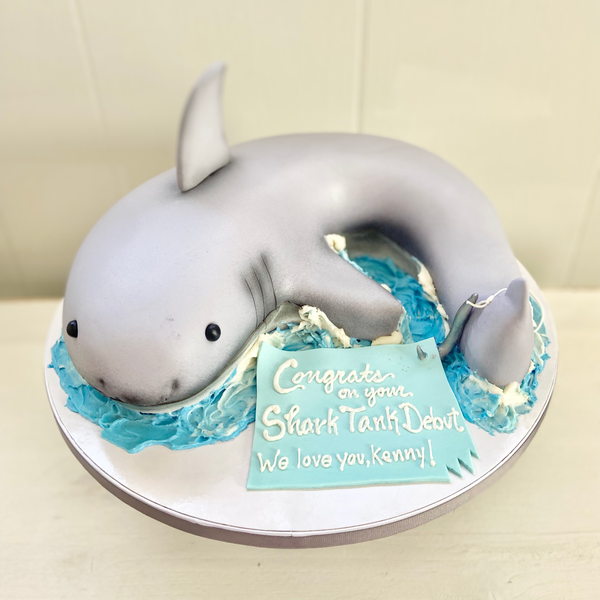 Cake shaped like a shark, featuring a congratulatory message.