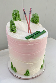 Cake with buttercream pine trees, fondant skis and ski poles on top.