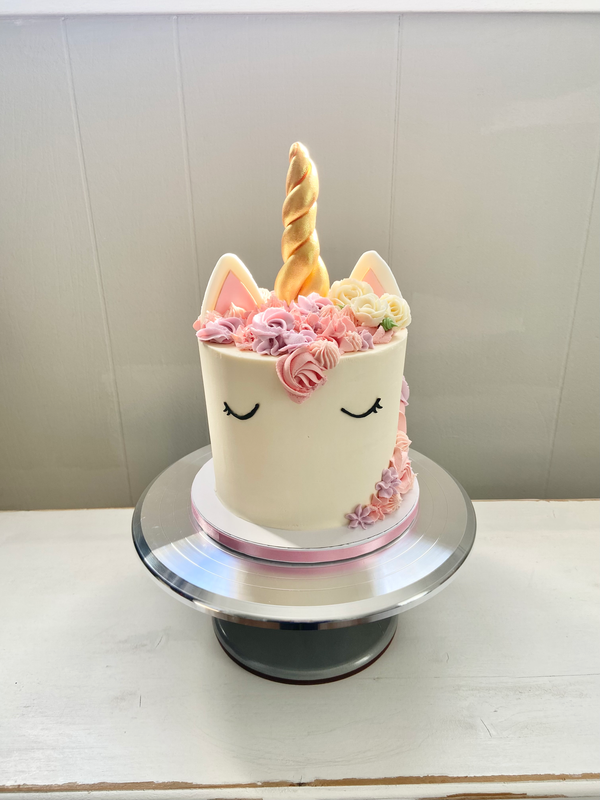 Cake with gold unicorn horn and ears on top, unicorn face on side, and floral mane.
