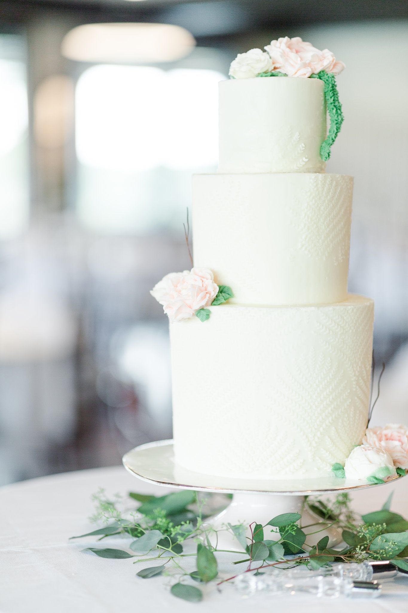 Three tiered white wedding cake with textured sides and pink buttercream flowers.